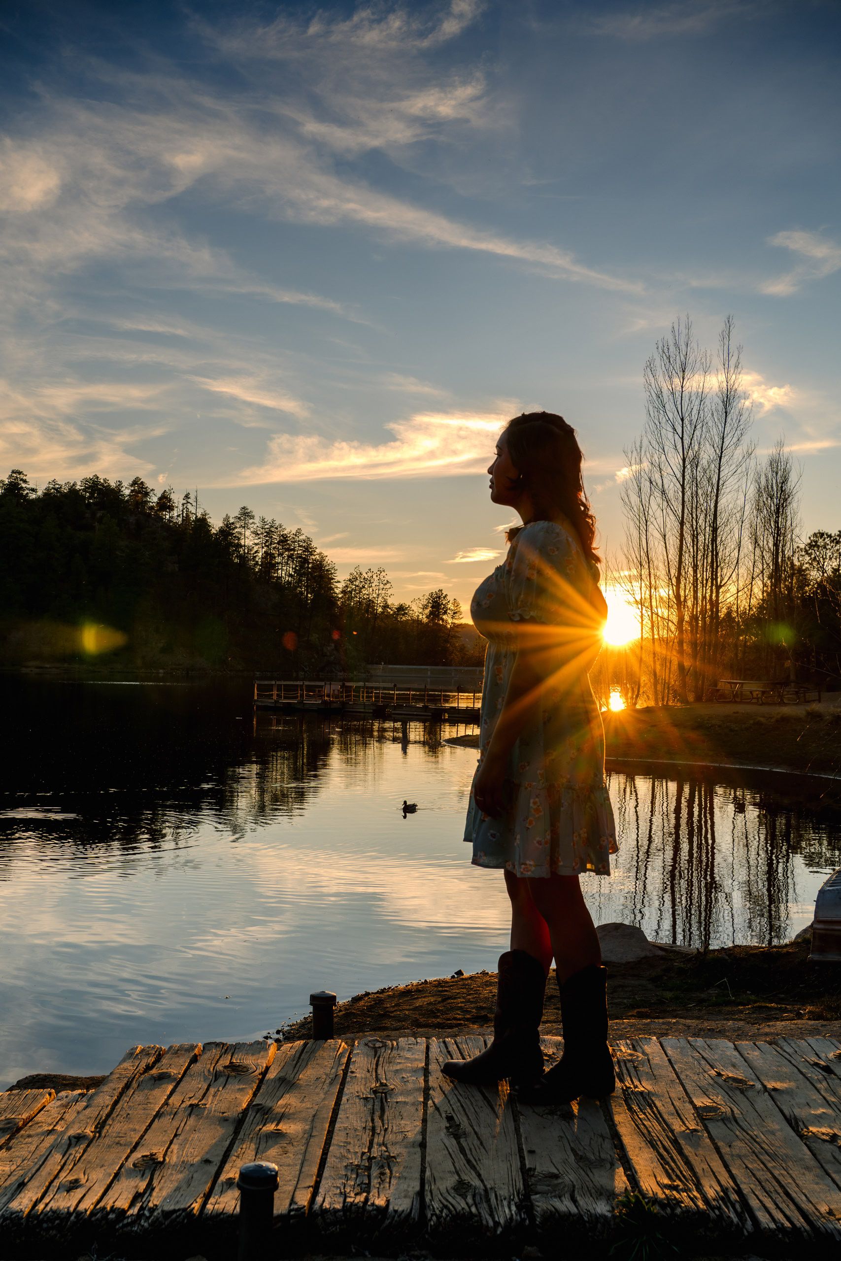 Woman standing on a rustic wooden dock at sunset overlooking a peaceful lake