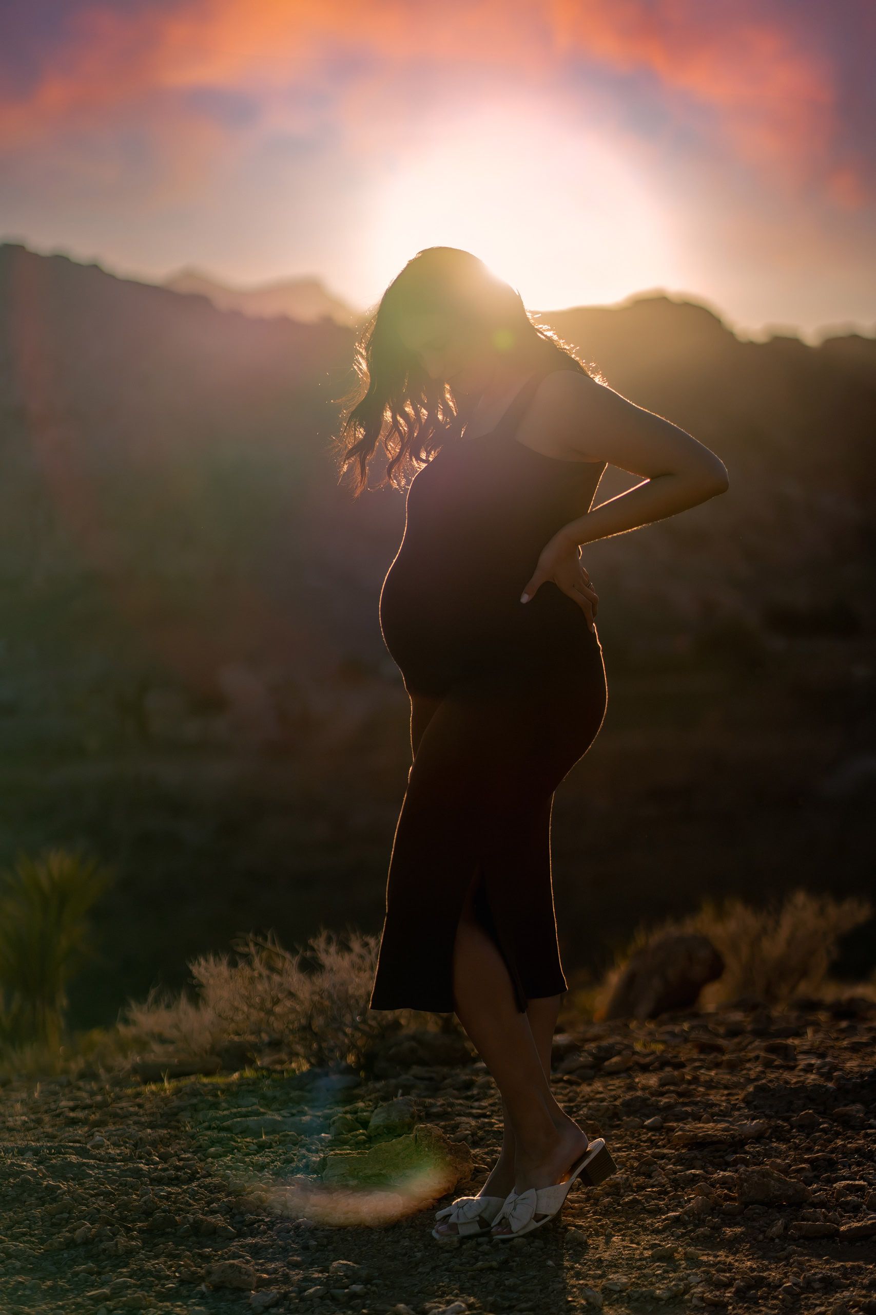 Sunset silhouette of an expectant mother against desert mountains and evening sky
